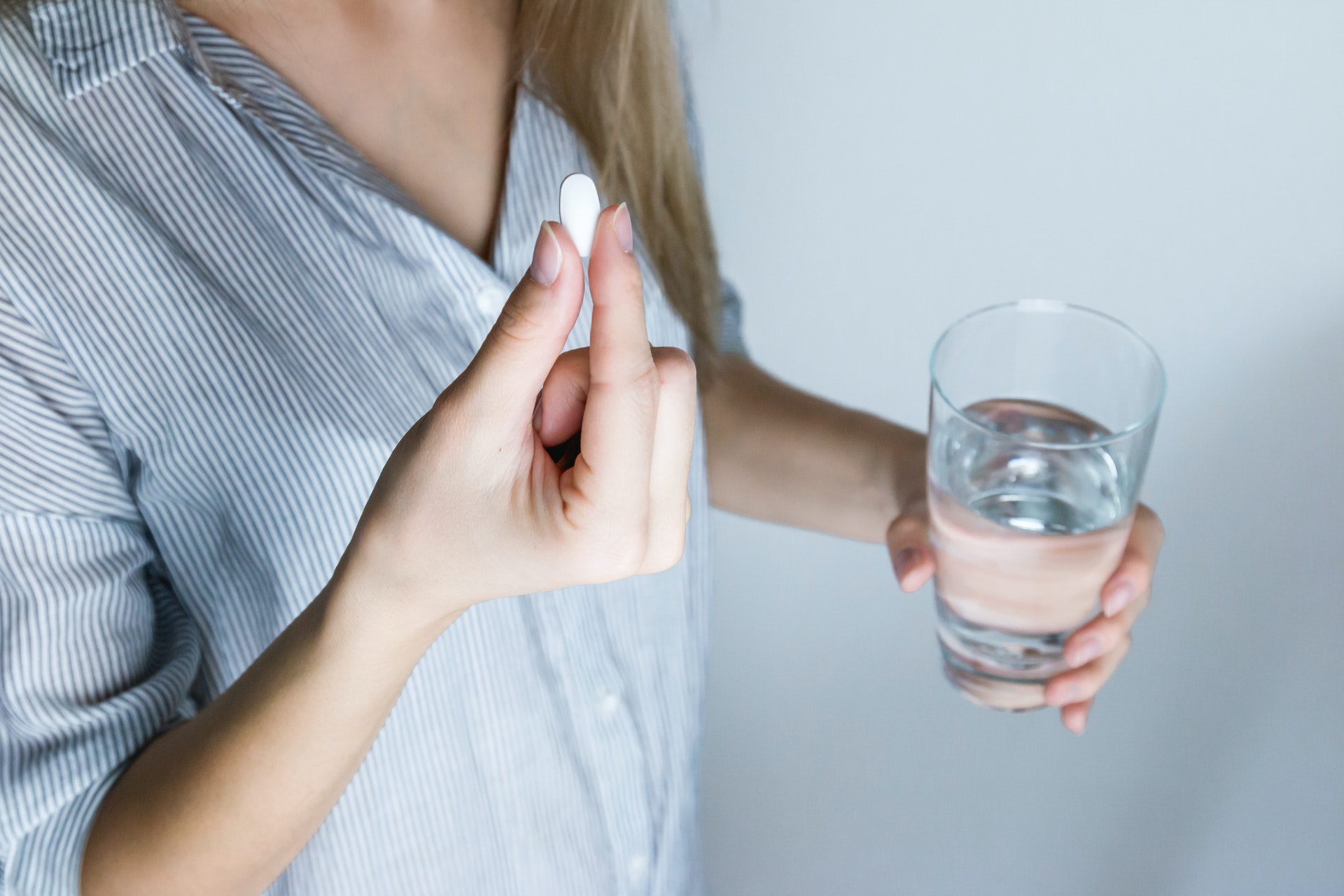 woman-holding-half-full-glass-and-white-medicine-pill