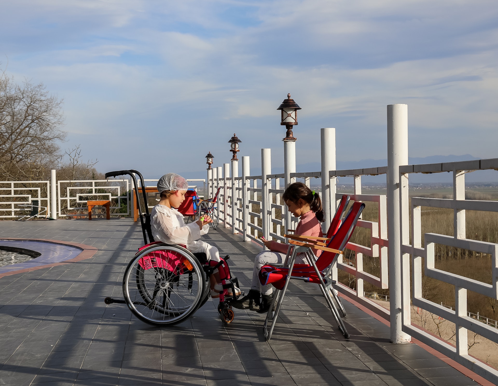 girl-resting-near-metal-railing-and-friend-in-wheelchair